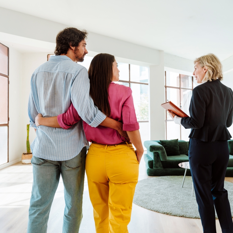 Real estate agent showing a new apartment and features of a good investment to a young couple. Woman and man buying a property in a rich area of the city.
